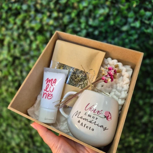 Kit em caixa kraft com caneca personalizada, sachê e flores secas, segurado na mão