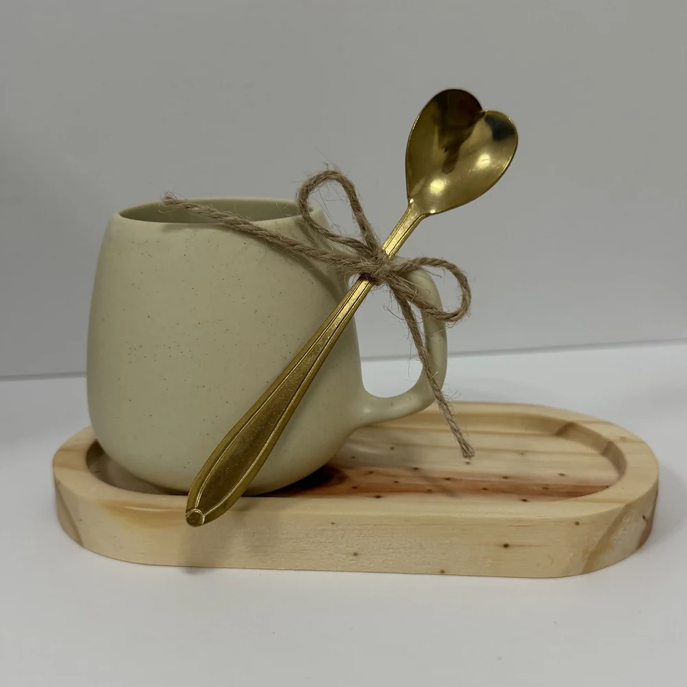 Caneca de porcelana creme com colher dourada de cabo em coração sobre pires de bambu