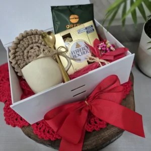 Caixa branca com laço vermelho contendo caneca creme, café Orfeu, bombom e descanso de crochê