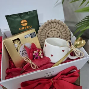 Kit de presente aberto com caneca de corações, café, bombons e flores secas sobre papel seda vermelho